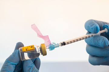 The hands of a sanitary in blue medical gloves ready to extract the COVID-19 vaccine from the ampoule with the syringe on a white background. COVID-19 preventive vaccination, coronavirus concept