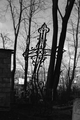 silhouette of a patterned cemetery cross against the background of trees and a cemetery, in black and white