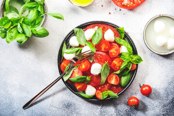 Summer caprese salad with red tomatoes and white mozzarella cheese with fresh green basil leaves. Gray table. Top view