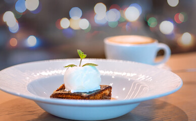 Chocolate cake with a ball of white ice cream decorated with mint leaf and caramel syrup is served on a large white plate in the restaurant. Restaurant menu.