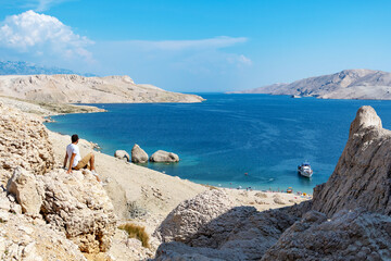 Young man sitting on cliff overlooking spectacular beach on Pag island in Croatia.