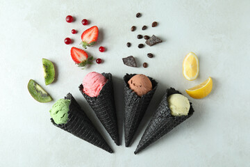 Black cones with ice cream and ingredients on white textured background