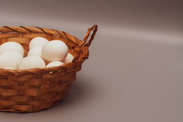 Wicker basket with white fresh chicken eggs on a gray background