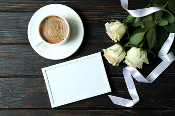 Roses, cup of coffee, empty frame and ribbon on wooden background