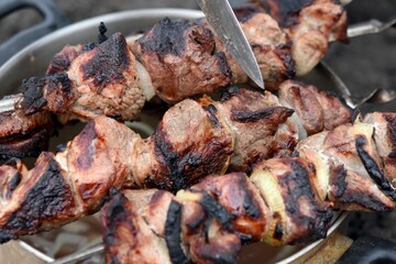 knife cuts pieces of fried kebab on a plate outdoors in summer