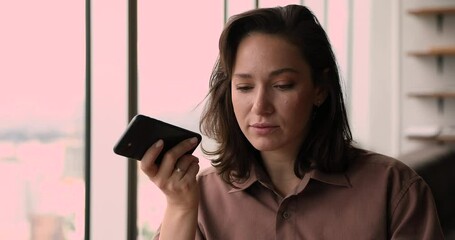 Attractive businesswoman sitting in office holding smartphone leave voice message, share voicemail to client, solve business issues talk to customer use speakerphone. Comfort modern tech usage concept
