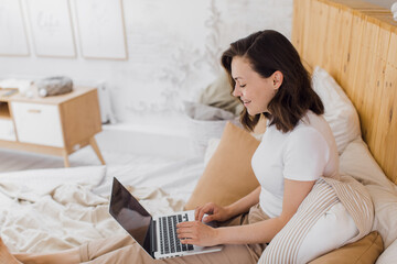 Fototapeta premium Woman Relaxing On Bed Using Laptop Computer For Video Call in modern flat