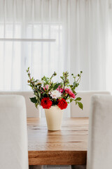 Dahlia flowers bouquet in a vase on wooden dining table. Modern room interior, bright and airy.