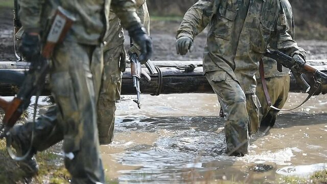 Special forces military training carrying a big log. Photograph detail with military equipment and assault rifle.