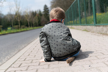 child sitting on pavement playing with stick