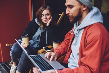 Obraz premium Female listening male during friendly distance working at modern laptop computer, skilled freelancers discussing business ideas for creating project planning collaboration at sidewalk terrace