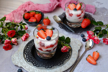 Obraz na płótnie Canvas Sweet dessert in glasses with berries - strawberries, blueberries and curd cream. Decorated with flowers - roses. Selective focus