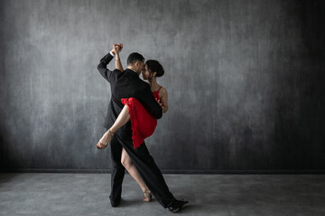 Couple of professional tango dancers in elegant suit and dress pose in a dancing movement on dark background. Attractive man and woman dance looking eye to eye. - obrazy, fototapety, plakaty