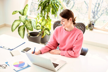 Young woman using laptop while sitting at desk and working