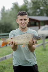 Happy angler holds trophy carp. Man with carp fish. Outdoors activities, fishing, catching fish concept