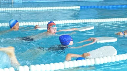 Children learn to swim with the help of a swimming board. A swimming instructor teaches children to swim in the pool. Teenagers in swimming suits learn to swim in the pool with an instructor