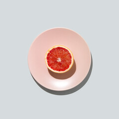 Fresh Grapefruit on pastel pink plate against gray background. Minimal summer flat lay concept.