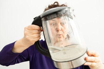Woman looks through transparent electric kettle with limescale. Concept chalk residue of calcium carbonate. Humor photo.