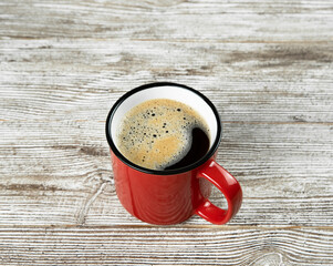 Red cup with black coffee on a brown wooden background.