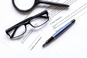 Fototapeta premium Pen and glasses lying on signed documents on office desk top view