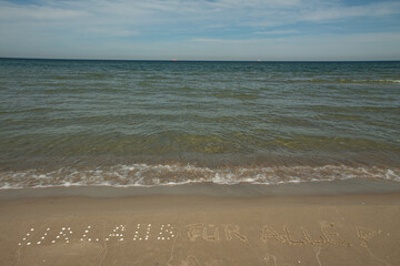 Fototapeta na wymiar Hintergrund mit Aufschrift im Sand, eine Forderung nach Urlaub für alle, an der ostsee mit Meer und wellen im Sommer 2021, während der Pandemie und corona
