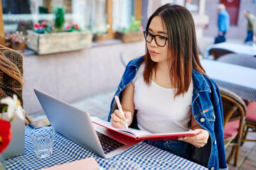 Focused Asian woman writing notes while studying