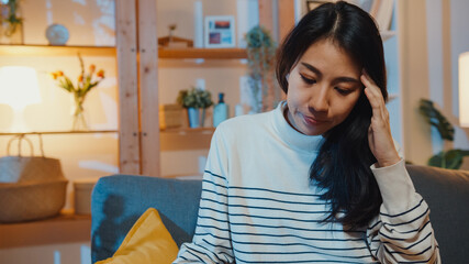 Obraz premium Thoughtful Asia lady suffering from insomnia sit at sofa in living room at house night with feel lonely, Sad depressed teenager spend time alone stay at home, Social distance, Coronavirus quarantine.