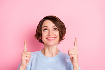 Photo of cheerful charming lady look direct fingers up empty space promo isolated on pink color...