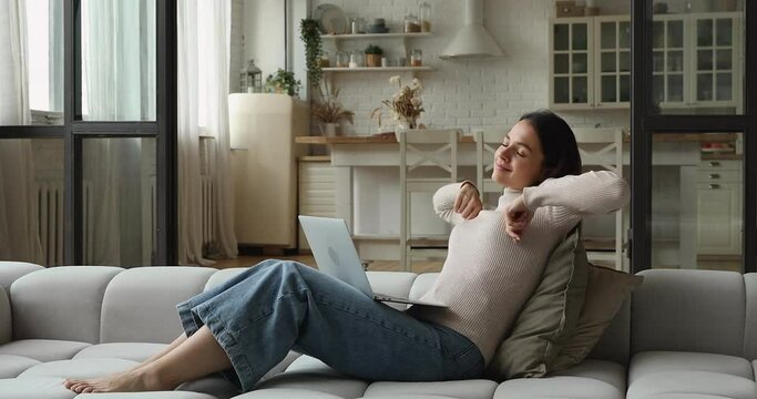 Young freelancer woman sit on comfy sofa at home finish work on laptop resting take break stretching back with raised arms, making exercised for muscles, feeling satisfied ending telecommuting concept