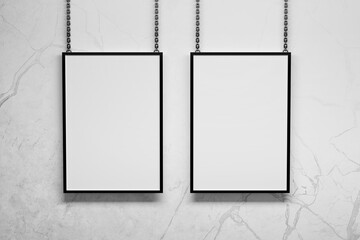 Two vertical A4 frames hanging on metallic chains next to wall