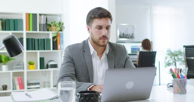Lateral dolly of young millennial professional using computer at office. Focused businessman thinking and typing on laptop. Busy worker freelancer working on modern tech notebook device. 
