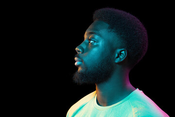 African young man's portrait on dark studio background in neon. Concept of human emotions, facial...