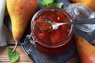 Homemade pear jam in a jar and fresh pears on a wooden background.