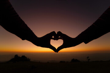 Silhouette hand heart shape with sunset.