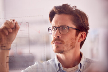 Male Architect In Office Making Notes On Building Blueprint On Transparent Screen