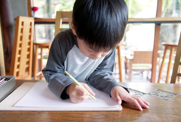 Little asian boy using a pencil to write on paper at the desk