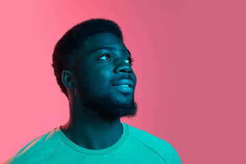 Obraz premium African young man's portrait on pink studio background in neon. Concept of human emotions, facial expression, youth, sales, ad.