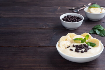 Healthy breakfast, dessert with milk yogurt banana and chocolate on a plate. Dark wooden background. copy space.