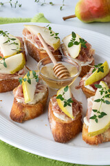 Close up of crostini appetizers topped with cream cheese, prosciutto and slices of pear, ready for eating.