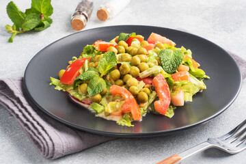 Salad of green tomato leaves and canned peas seasoned with sauce on a black plate. Spring fresh diet salad. top view