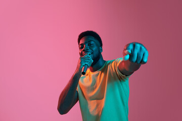 African young man's portrait on pink studio background in neon. Concept of human emotions, facial expression, youth, sales, ad.