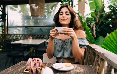 Satisfied ethnic lady with cup of coffee in tropical garden