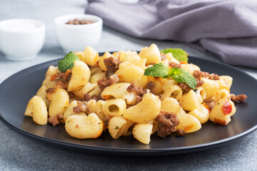 Stewed pasta with minced beef and vegetables, macaroni in Navy style on a plate. grey concrete background.