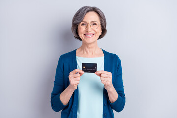 Photo of charming attractive positive old woman hold hands credit card good mood isolated on grey color background