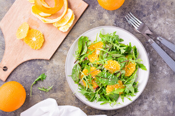 Diet vegetarian vitamin salad of orange slices and a mix of arugula, chard and mizun leaves on a plate and a cutting board with peeled orange on the table. Top view
