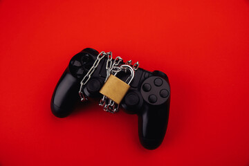 Gamepad with chain and padlock on red background, game addiction concept.