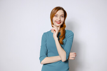 Portrait of a cheerful, thoughtful red-haired woman in a blue dress on a white background. Copy space.