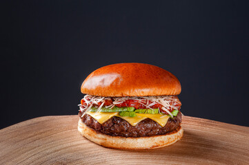 .Delicious beef burger with tomato sauce, parmesan cheese and lettuce on wooden table on dark...