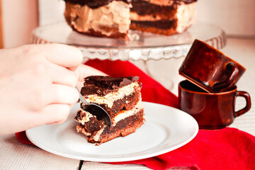 Slice of three chocolate cake on a plate. Delicious tasty homemade cake on table. White wooden background. Young woman eating dessert process