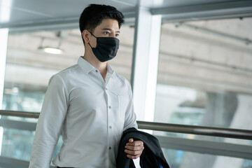 Asian business man wearing protective mask carrying luggage and suit walking to airport terminal. people travel for business trip during Coronavirus crisis. copy space